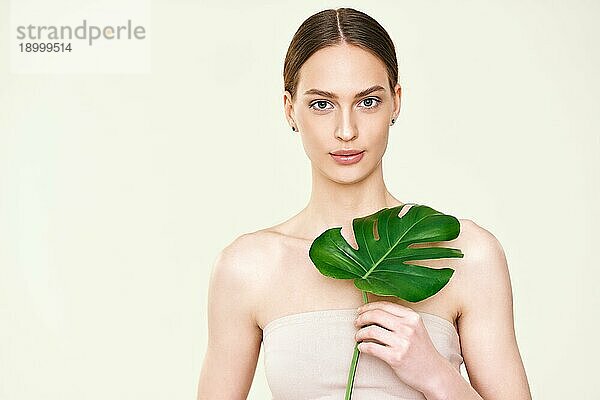 Junge schöne Frau hält monstera tropischen Blatt mit Kopie Raum. Naturkosmetik  Hautpflege  Spa und weibliche Schönheit Konzept