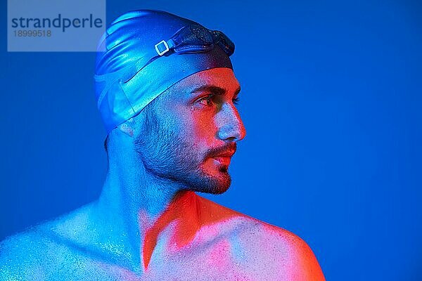 Close up Profil Porträt von gut aussehend Schwimmer mit Schwimmbrille in rot rosa Neonlicht über blaün Hintergrund mit Kopie Raum. Sport  Mode  männliche Schönheit