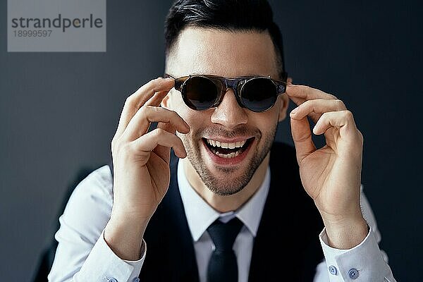 Glücklicher lachender Mann mit Retro Sonnenbrille auf schwarzem Hintergrund. Spaß Konzept