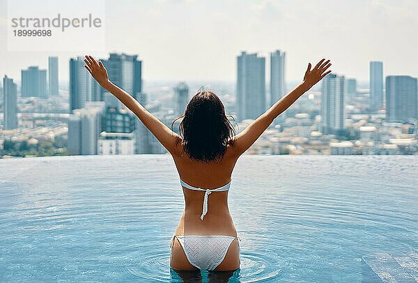 Zurück Blick auf glückliche Freiheit Frau mit erhobenen Armen genießen ihren Sommerurlaub am Swimmingpool auf dem Dach des Hotels. Reisen  Urlaub  Erfolg Konzept
