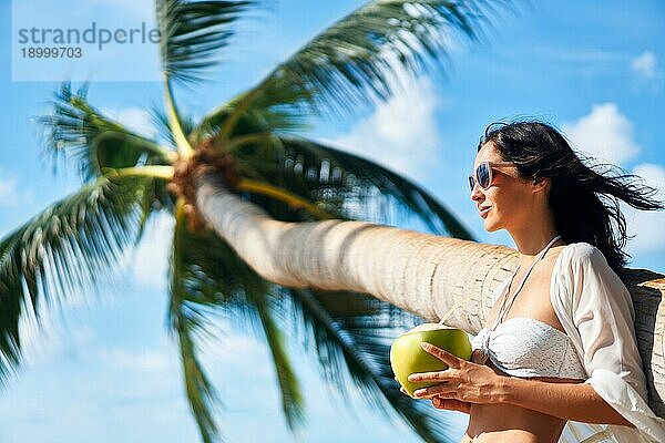 Schöne junge Frau genießen Kokosnuss Getränk und entspannen am tropischen Strand mit Palme. Sommerurlaub Konzept