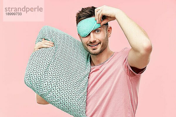 Lustige fröhliche Mann in Schlafmaske hält Kissen in den Händen Blick in die Kamera über rosa Hintergrund. Entspannen  guten Morgen Konzept