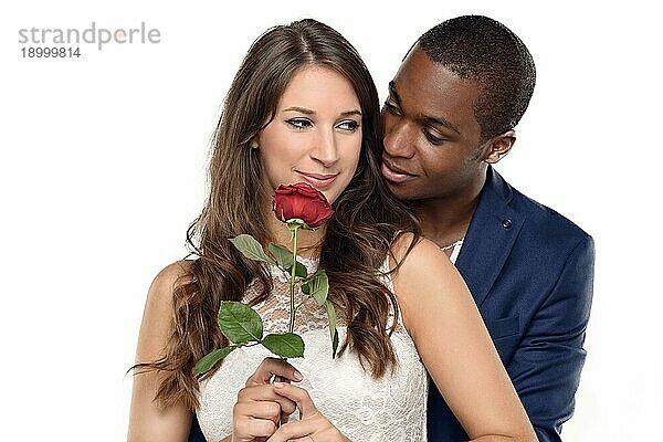 Hübscher schwarzer amerikanischer Freund  der seine hübsche Freundin mit einer Rosenblüte umarmt und in die Kamera lächelt  in der Küche stehend