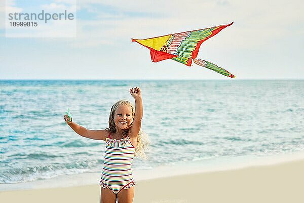 Glückliches kleines Mädchen mit fliegendem Drachen am tropischen Strand. Strand Spaß  Kindheit Konzept