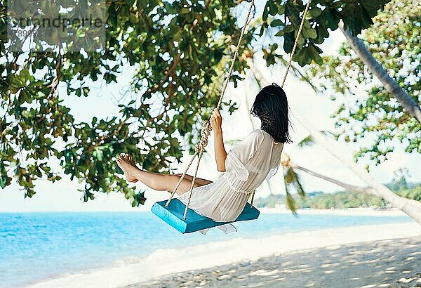 Sorglose glückliche Frau auf einer Schaukel an einem paradiesischen Strand. Entspannung und Freiheit Konzept
