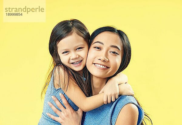 Glückliche Mutter und ihr Kind Tochter umarmen auf gelbem Hintergrund. Familie  umarmen Konzept