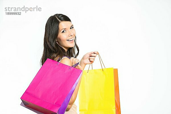 Glückliche Frau beim Einkaufen mit bunten Taschen voller neuer Einkäufe  die sich umdreht  um in die Kamera zu lächeln  mit einem Blick der Zufriedenheit und Freude