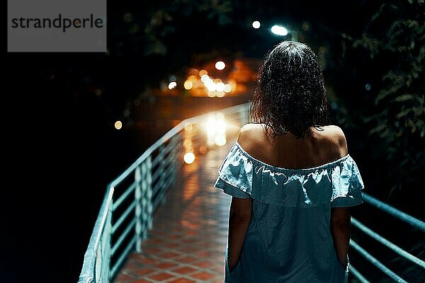 Rückenansicht einer jungen einsamen Frau  die nachts auf der Brücke spazieren geht