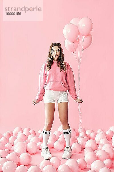 In voller Länge Porträt von trendy überrascht Mädchen mit rosa Luftballons auf rosa Pastell Hintergrund. kreatives Konzept. Menschen Emotionen