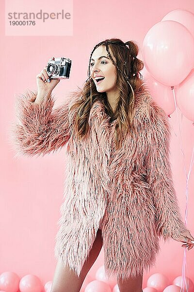 Pretty glücklich Glamour Frau  die Foto mit Retrokamera über rosa Luftballons Hintergrund. Party Konzept