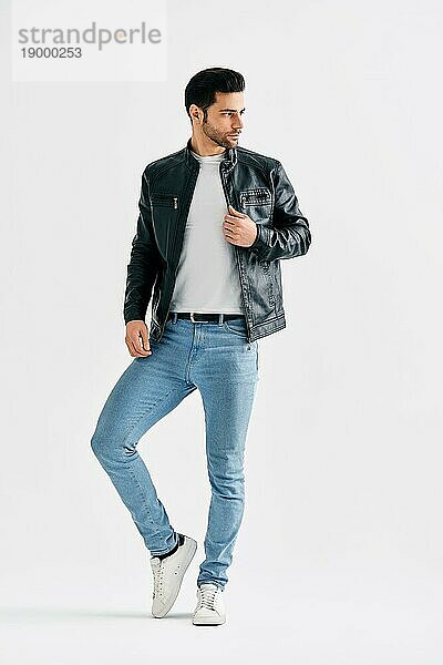 Handsome stilvollen Männchen Porträt auf weißem Hintergrund Studio. Men's Schönheit Konzept. Junger Männchen trägt Jeans  weißes TShirt und schwarze Lederjacke posiert in voller Länge