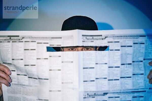 Mann versteckt Uhren durch die Zeitung im Scheinwerferlicht auf Studio Hintergrund. noir Film Stil. Privatdetektiv  Untersuchung  Geheimnis  Detektiv  Spionage Konzept