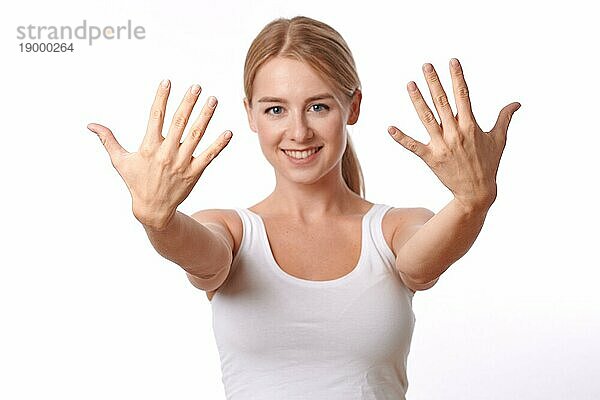 Lächelnde freundliche junge Frau  die ihre Hände mit gespreizten Fingern in Richtung der Kamera zeigt  vor weißem Hintergrund