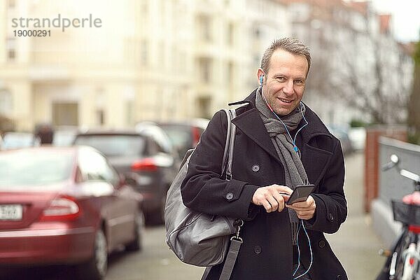 Attraktiver Mann in Wintermode  der auf einer städtischen Straße steht und sein Mobiltelefon auf Nachrichten überprüft oder einen Anruf tätigt  Nahaufnahme des Oberkörpers