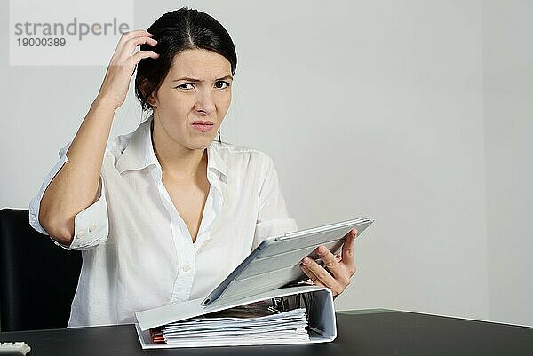 Eine verwirrte Frau kratzt sich am Kopf und zieht eine Grimasse  während sie versucht  eine Antwort auf ein Problem zu finden  das ihr auf ihrem Tabletcomputer gestellt wurde