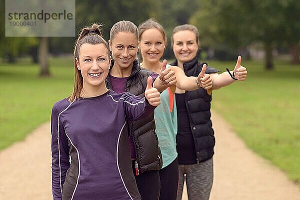 Vier glückliche  gesunde junge Frauen in der Schlange  die nach ihrer Outdoor Übung den Daumen in die Kamera halten