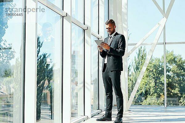 Ganzes Porträt eines lächelnden Geschäftsmannes  der in einem modernen Kreativbüro an einem Tablet arbeitet