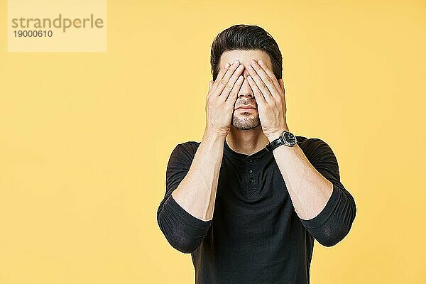 Porträt von gestressten müden Mann schloß die Augen von zwei Händen über gelben Hintergrund. emotion Konzept