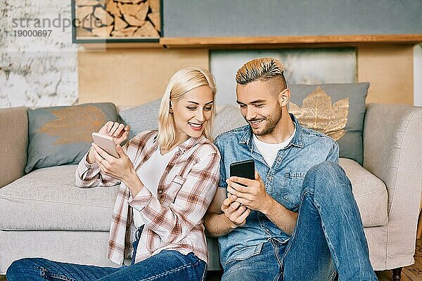 Lächelndes junges Paar entspannt sich auf der Couch mit Smartphone zu Hause. Glücklich zusammen