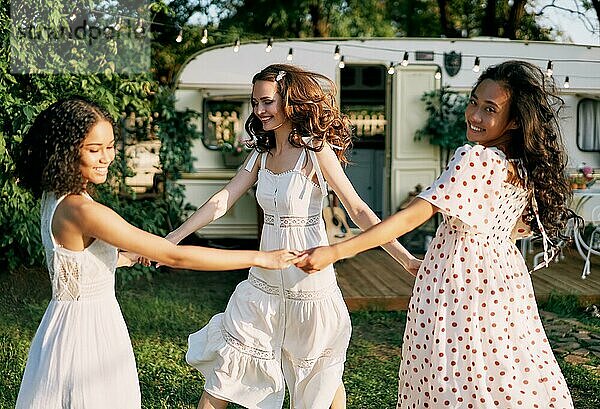 Glückliche schöne Frauen tanzen im Kreis während eines Picknicks. Multi ethnischen Mädchen Spaß haben zusammen im Freien. Kaukasische  afroamerikanische und asiatische Mädchen genießen den Urlaub. Frauen Freundschaft und Frauen Schönheit Konzept