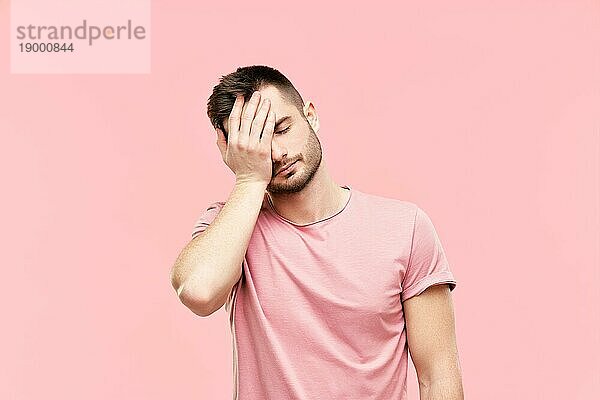 Müde enttäuschten jungen Mann mit Gesicht Palm Geste über rosa Hintergrund. Emotion Konzept