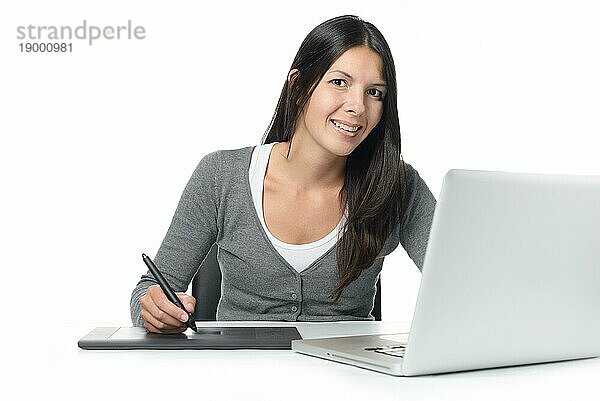 Weibliche Grafikdesignerin lächelt  während sie ihre kürzlich heruntergeladenen Dateien auf einem Laptop mit einem Grafiktablett bearbeitet  vor weißem Hintergrund