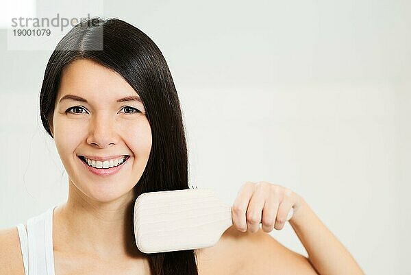 Attraktive Frau bürstet ihr Haar und schaut mit einem freundlichen  charmanten Lächeln in die Kamera