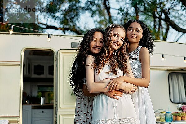Schöne multiethnische Mädchen umarmen in der Nähe Wohnmobil im Freien. Beste Freunde Mädchen haben Spaß zusammen bei einem Picknick. Frauen Freundschaft und Frauen Schönheit Konzept