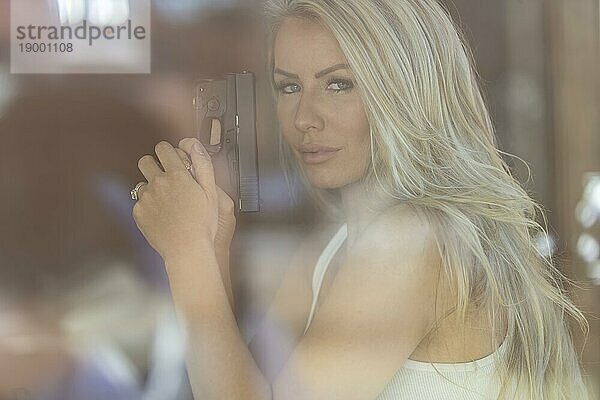 Ein schönes blondes Modell hält eine Pistole zum Schutz an einem sonnigen Tag