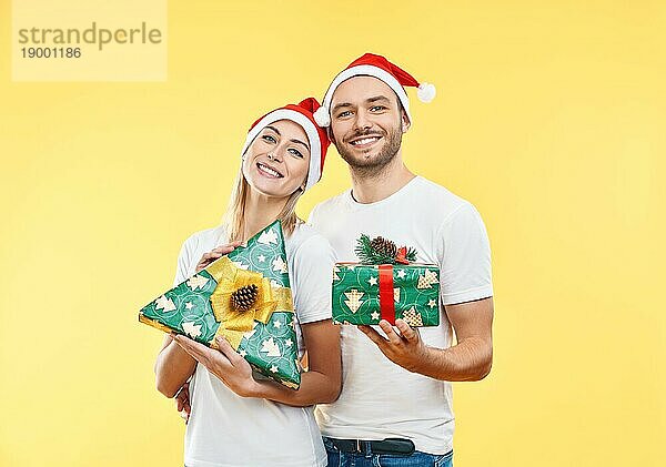 Junges glückliches Paar mit Weihnachtsgeschenkboxen auf gelbem Hintergrund. Geschenk  Urlaub  Feier Konzept