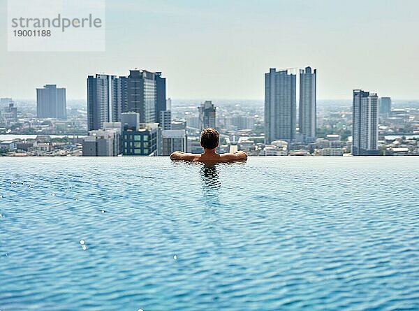 Junger Mann entspannt sich am Rande des Dachterrassenpools. Sommerurlaub Konzept