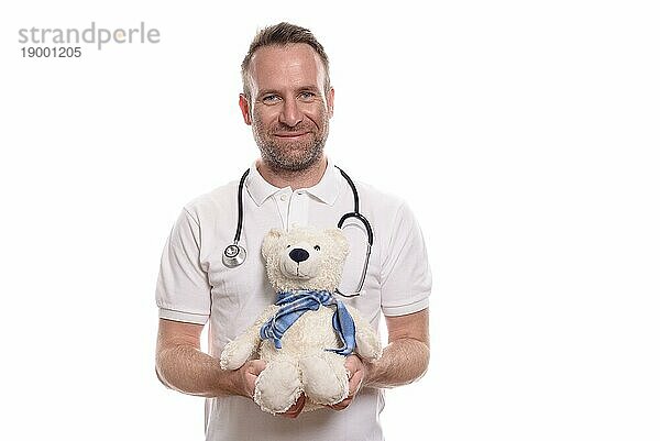 Lächelnde Kinderärztin oder männlicher Kinderkrankenpfleger  die der einen niedlichen  ausgestopften Teddybären hält  während er versucht  einen jungen Patienten auf der Krankenhausstation zu trösten und zu beruhigen  vor weißem Hintergrund