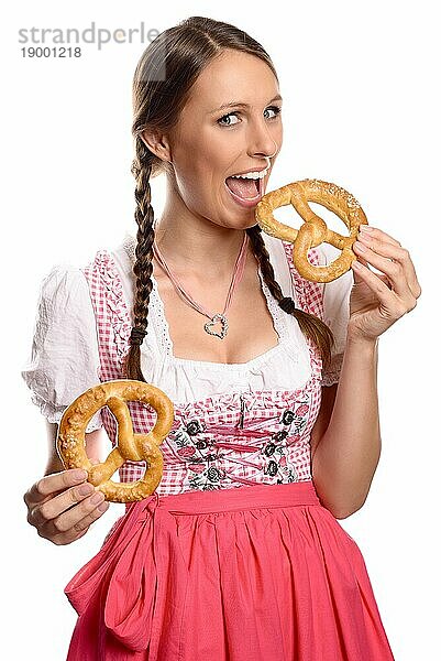 Glückliche attraktive junge deutsche oder bayerische Frau im Dirndl  die zwei Brezeln in der Hand hält und den Mund weit öffnet  um einen Bissen zu nehmen  vor weißem Hintergrund