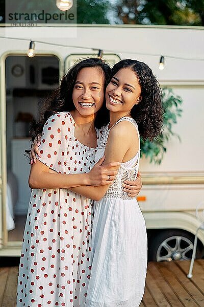 Glücklich lächelnd asiatischen und afroamerikanischen Frau umarmen und haben eine tolle Zeit zusammen. Frauen Freundschaft Konzept. Zwei beste Freunde umarmen im Freien