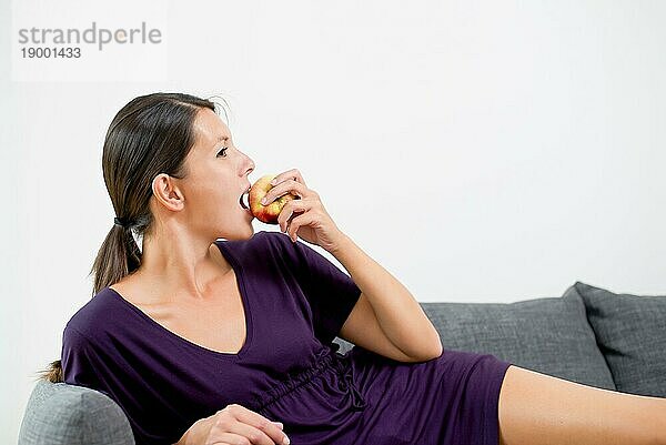 Seitenansicht einer attraktiven jungen Frau  die in einen frischen  saftigen  roten Apfel beißt  da sie eine gesunde Ernährung und Lebensweise verfolgt