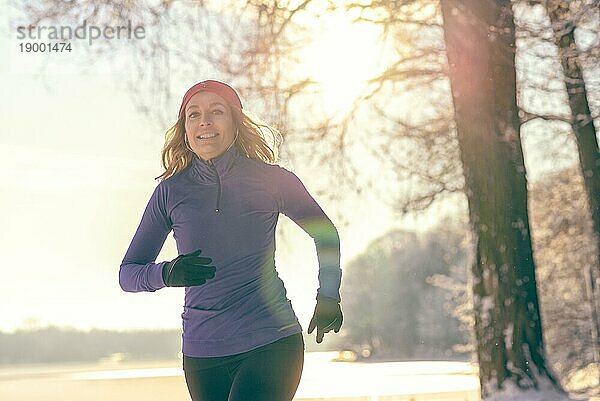 Ganzkörperaufnahme einer hübschen sportlichen Frau beim Joggen im Winter mit Kopfhörern und Winterkleidung  die in die Kamera lächelt  mit Kopiervorlage