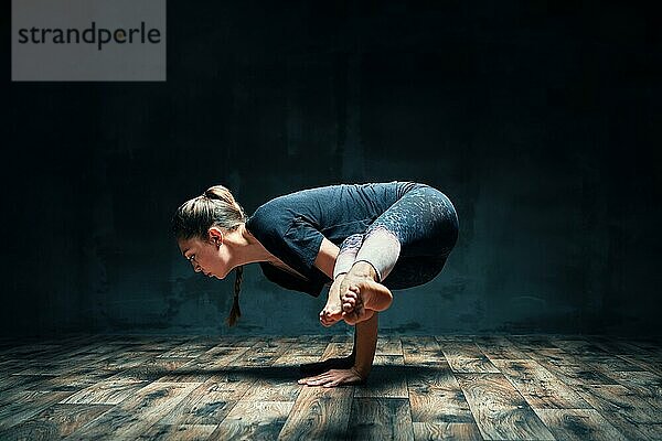 Junge attraktive Frau übt Yoga tun Seite Kranich Pose in dunklen Raum. Parsva Bakasana Übung. Gleichgewicht und Erholung Konzept