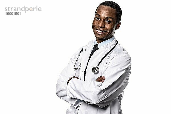 Attraktiver selbstbewusster männlicher afrikanischer Arzt in weißem Laborkittel und Stethoskop  der mit einem glücklichen Gesichtsausdruck in die Kamera schaut  Oberkörper vor weißem Hintergrundem Grund
