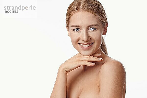 Schöne gesunde junge Frau voller Vitalität  die ihre Hände an ihre Wangen hält  um ihre Brüste zu schützen  während sie der Kamera ein strahlendes Lächeln schenkt