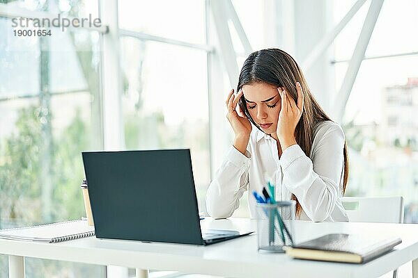 Gestresste müde Geschäftsfrau sitzt an ihrem Schreibtisch in einem modernen Büro. Probleme  Schmerz Konzept