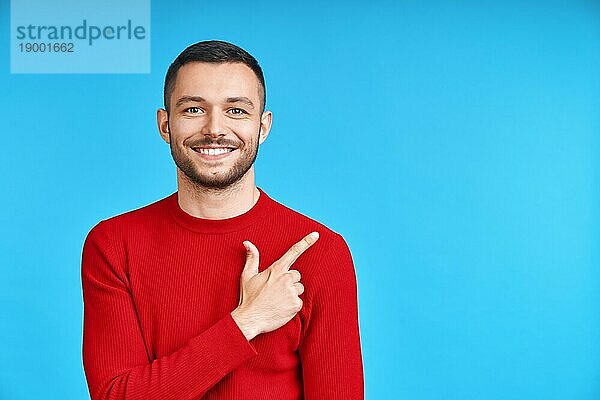 Gutaussehender  glücklicher Mann zeigt mit dem Finger auf leeren Kopierraum  vorblauem Hintergrund. Präsentiert Produkt und Werbekonzept