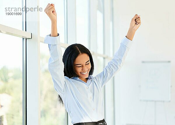 Porträt einer glücklichen  aufgeregten schwarzen Geschäftsfrau mit erhobenen Armen  die ihren Erfolg in einem modernen  kreativen Büro feiert