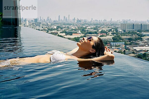 Junge Frau entspannt sich am Rande des Dachterrassenpools. Sommerurlaub Konzept