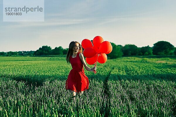 Freiheit glückliche Frau läuft mit roten Luftballons auf grünem Sommerfeld. Spaß  Glück Konzept
