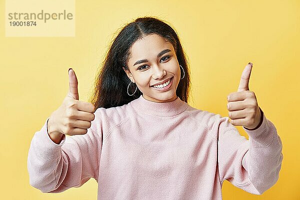 Lächelnde hübsche Frau zeigt Daumen hoch Zeichen über gelben Hintergrund. Gewinner  Erfolg Konzept