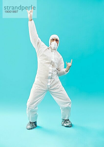 Full lenght Porträt von glücklichen Arzt in PSA Anzug feiert seinen Erfolg mit Sieger Geste und Hände hoch auf blauem Hintergrund. Sieg  Triumph und Emotionen Konzept