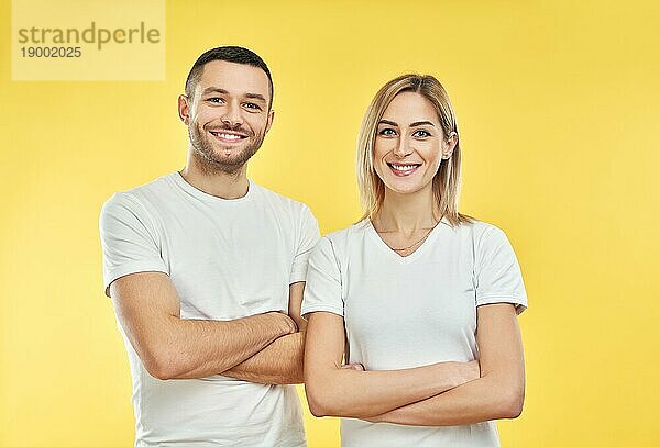 Junges glückliches Paar mit gekreuzten Armen auf gelbem Hintergrund. Lächelnder Mann und Frau posieren im Studio