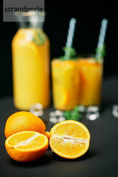 Leckerer frischer Orangensaft mit Eis  Minze und Früchten auf schwarzem Tischhintergrund. Fokus auf Früchte. Party  Getränk  Gesundheit Konzept