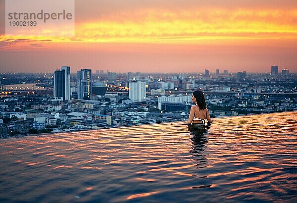 Junge Frau entspannen im Schwimmbad auf dem Dach während erstaunlichen Sonnenuntergang und genießen Stadtbild. Sommerurlaub und Ferien Konzept