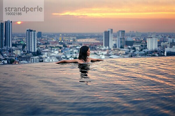 Junge Frau entspannen im Schwimmbad auf dem Dach während erstaunlichen Sonnenuntergang und genießen Sie den Blick auf die Stadt. Sommerurlaub und Ferien Konzept